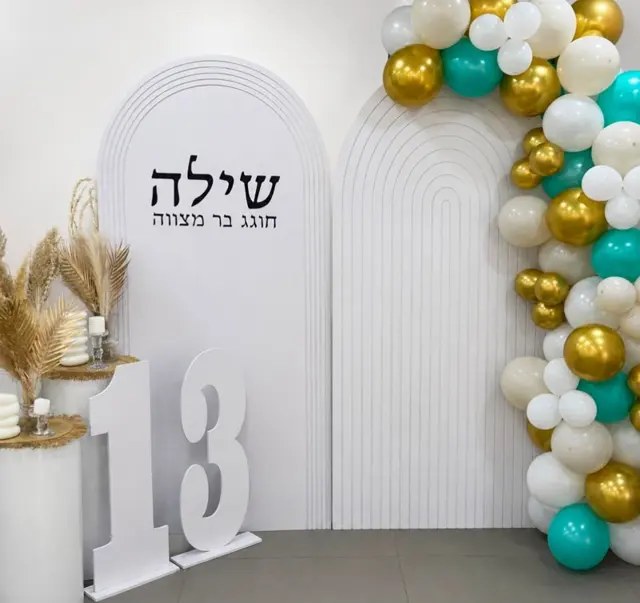קיר צילום עם קשתות לבנות, שם החוגג, מספר 13 ושרשרת בלונים בזהב, טורקיז ולבן